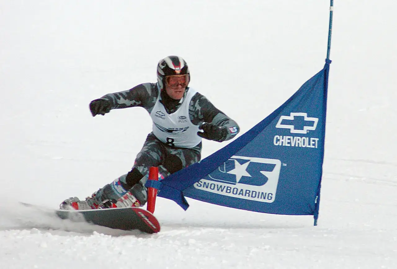 Snowboardzista w kasku i goglach mija niebieską flagę z logo Chevrolet. To sport, który zyskał popularność w XX wieku, choć jego korzenie sięgają wcześniejszych lat.