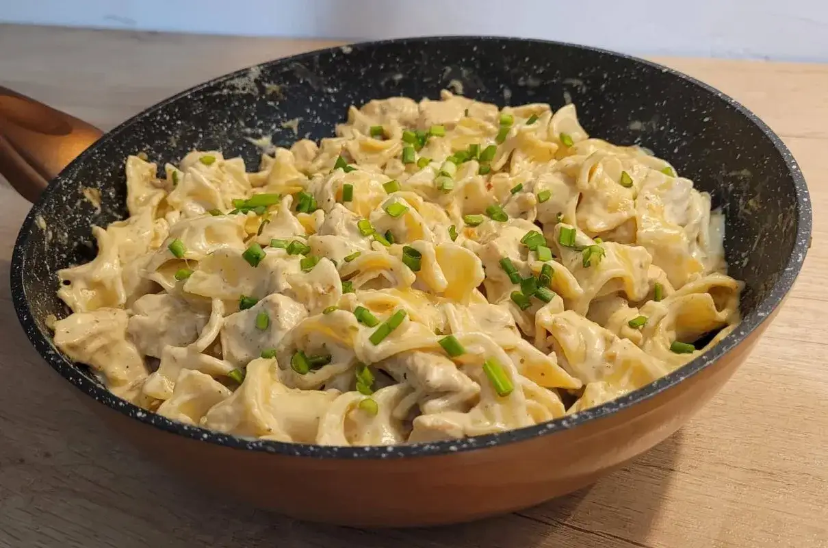 Tagliatelle z kurczakiem w sosie śmietanowym, posypane szczypiorkiem, podane w patelni. Pyszne danie gotowe do spożycia.