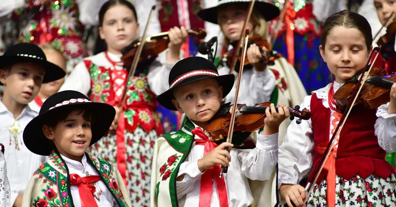 Dzieci w strojach ludowych grają na skrzypcach.