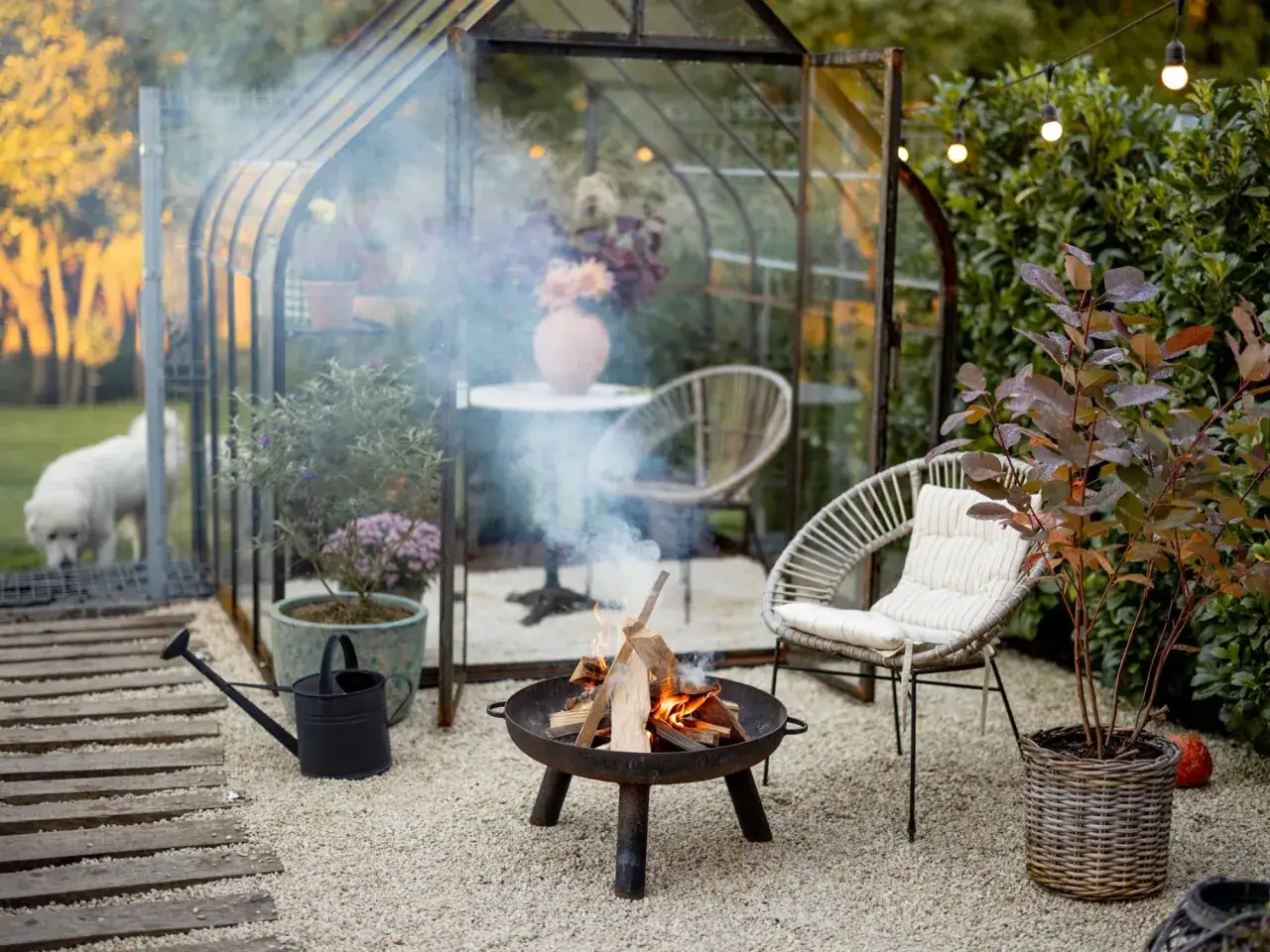 Ognisko w metalowej misie na żwirze, obok szklarni i krzesła.