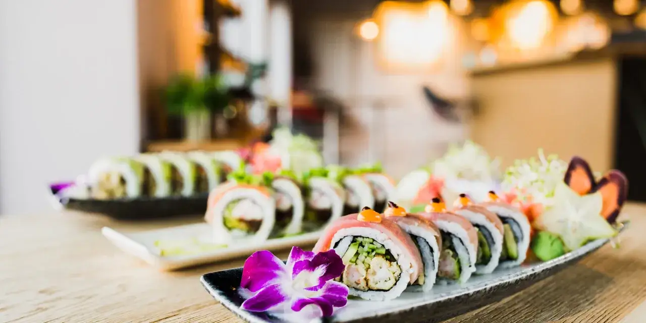 Wykwintne sushi z mięsem, ozdobione kwiatem i warzywami, prezentuje się apetycznie na talerzu.