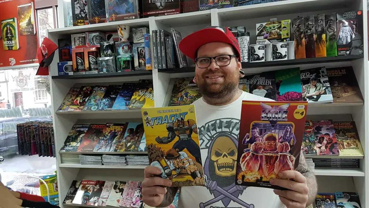 Mann mit Brille und roter Kappe hält zwei Comics in einem Comicladen.