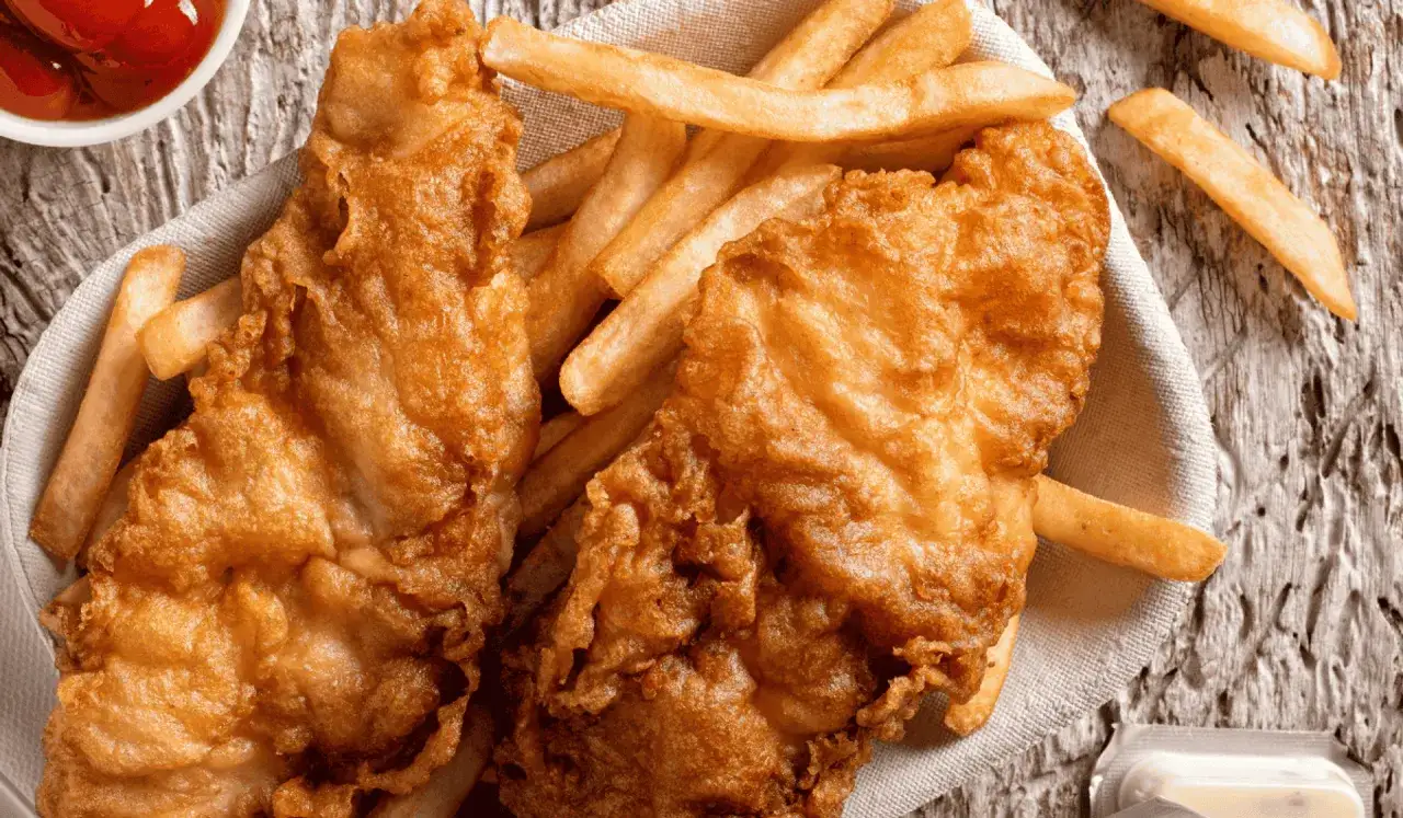 Chrupiący smażony filet rybny z frytkami na drewnianym tle.