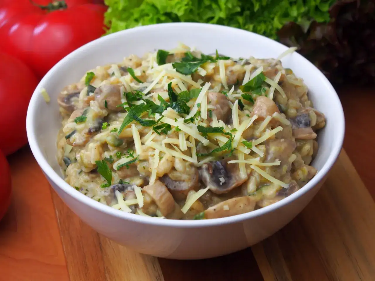 Pyszne risotto z pieczarkami, posypane startym serem i świeżą natką pietruszki, czeka w białej miseczce.