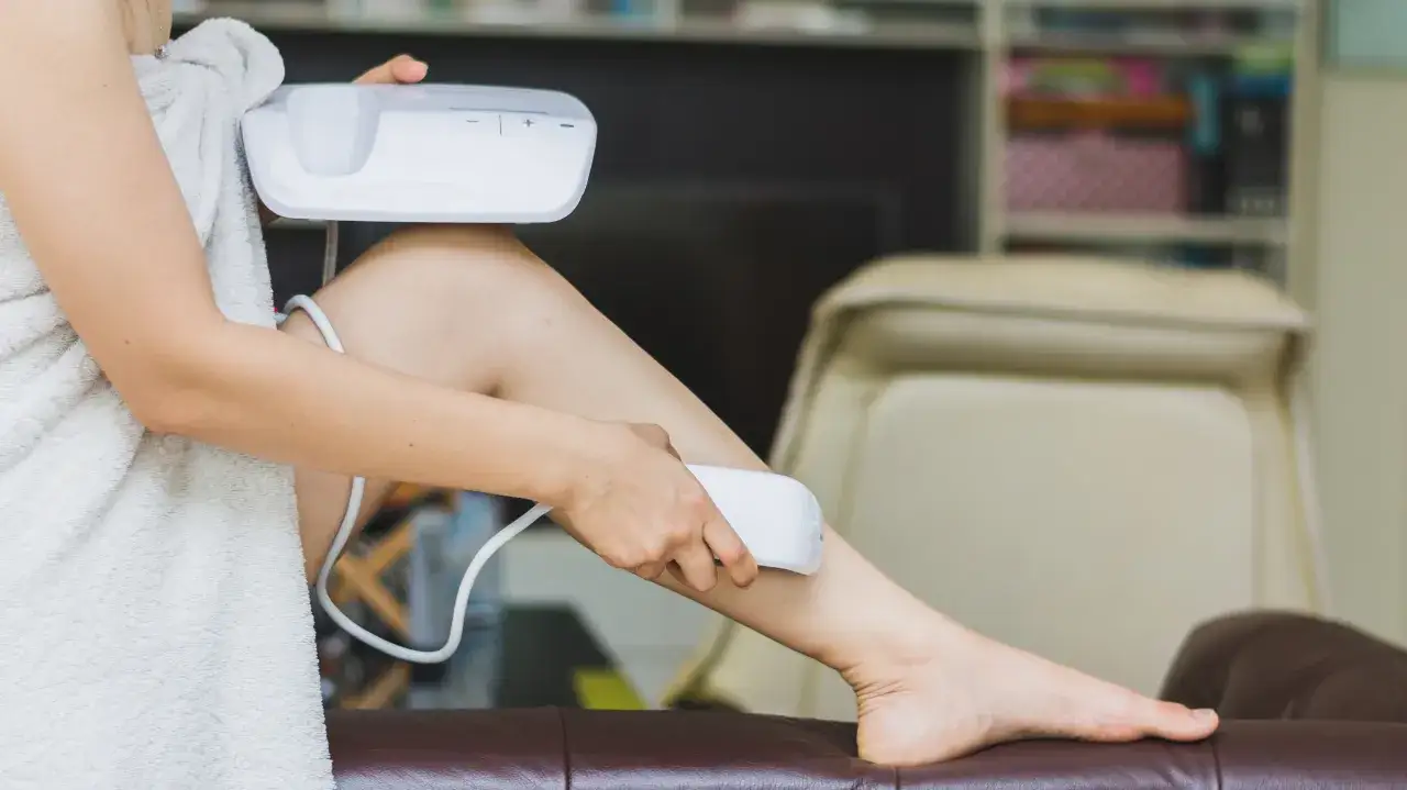 Kobieta owinięta ręcznikiem używa białego depilatora na nogę.