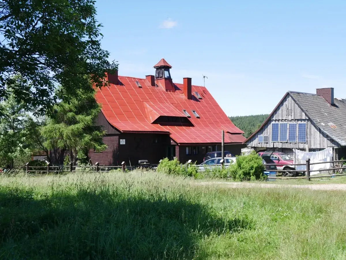 Górzyste krajobrazy, gdzie króluje chatka górzystów z czerwoną dachem. Wokół zieleń i kilka samochodów.