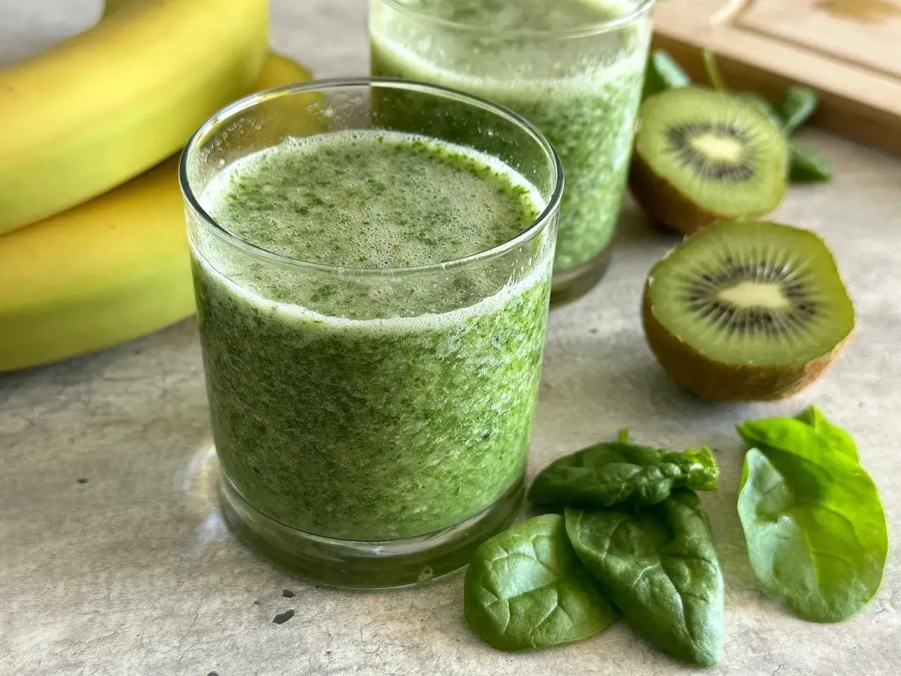 Orzeźwiający koktajl ze szpinakiem, bananami i kiwi. Zielony napój w szklance, obok świeże liście szpinaku i owoce.