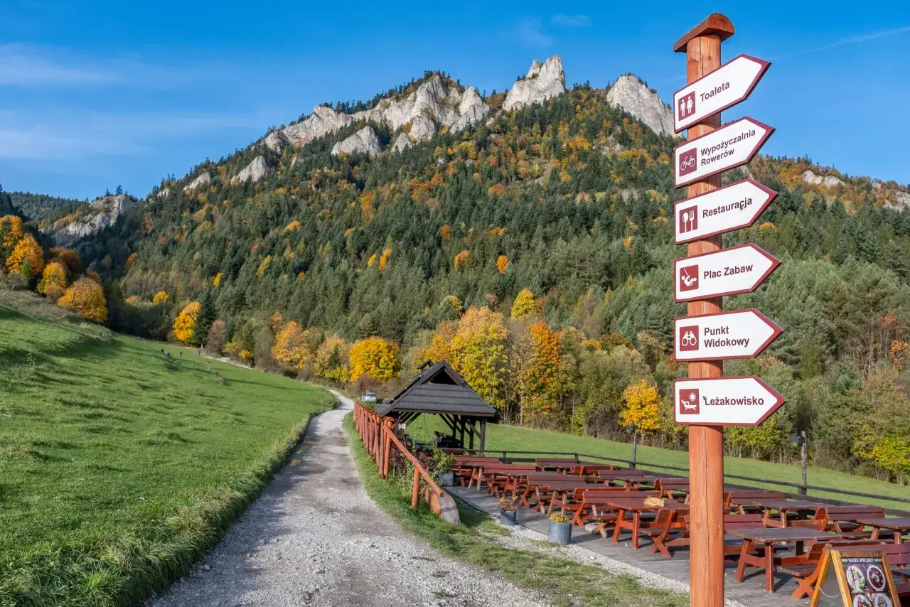Jesień w Pieninach, szlak do Trzech Koron. Droga prowadzi przez łąkę i las, a tabliczka informuje o atrakcjach.