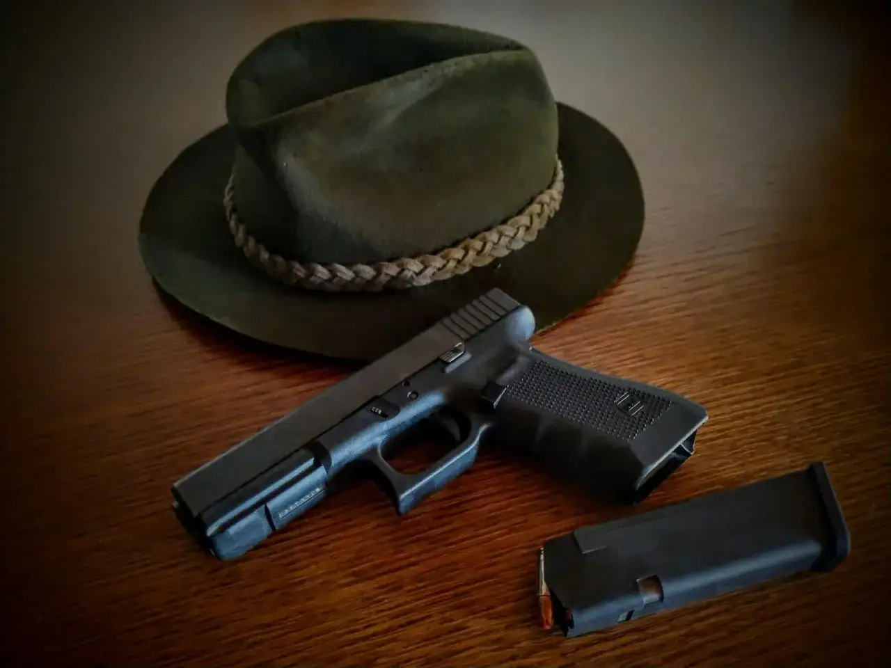 Na drewnianym stole leży ciemnozielony kapelusz myśliwski i pistolet z magazynkiem. Czy myśliwi mogą posiadać broń krótką?