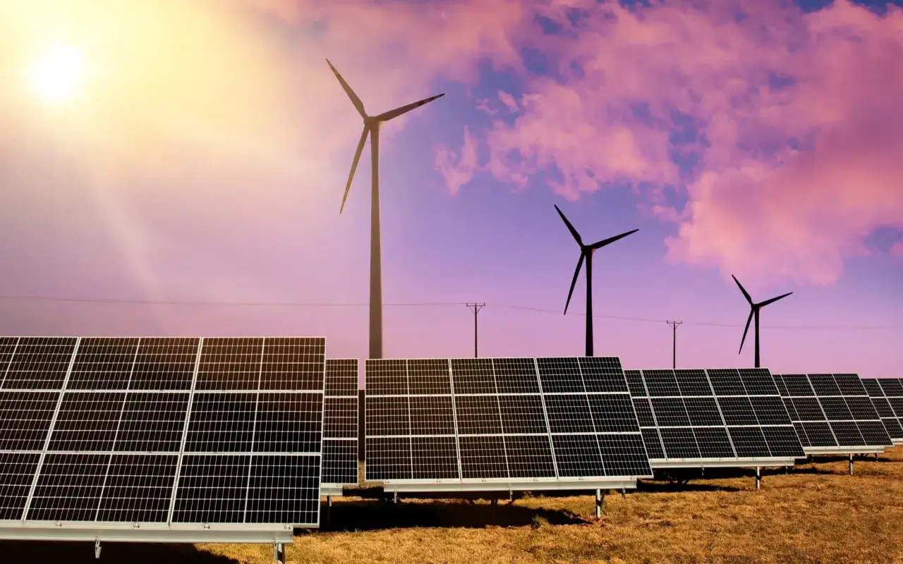 Panele słoneczne i wiatraki na tle zachodzącego słońca.