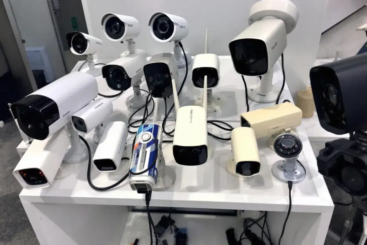 Plusieurs caméras de surveillance extérieures sans fil de différents modèles et couleurs sont exposées sur un présentoir blanc.