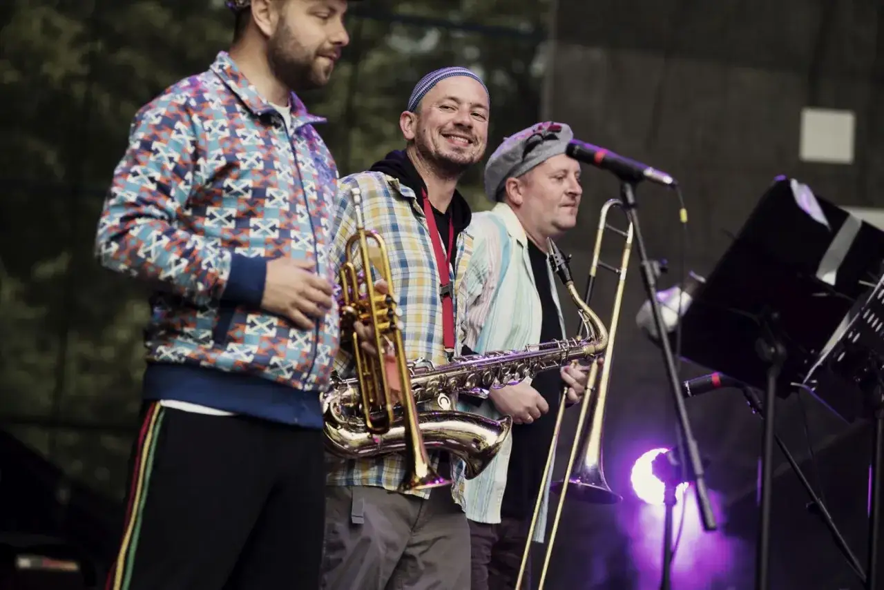 Adam Kłosiński z zespołem na scenie, grają na saksofonie i puzonie.