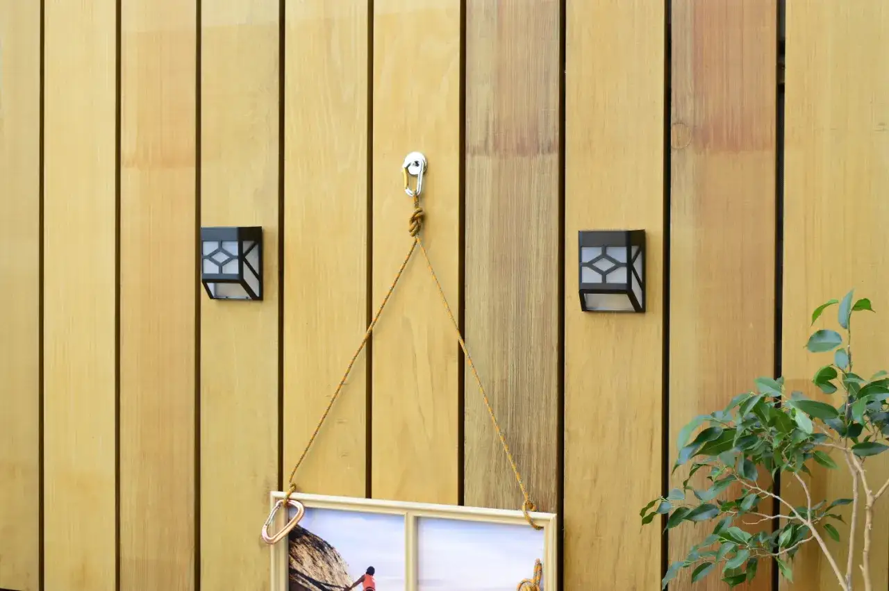 Dwie lampy na taras solarne oświetlają drewnianą ścianę, na której wisi obraz.
