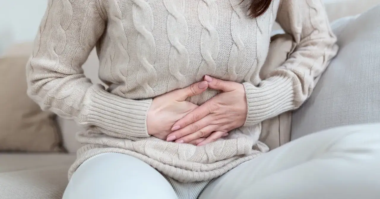 Kobieta trzyma się za brzuch, cierpiąc z powodu bólu brzucha po alkoholu. Co robić w takiej sytuacji?