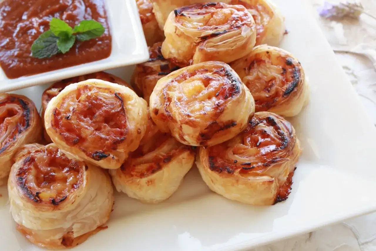 Pyszne przekąski na andrzejki: zawijane roladki z ciasta francuskiego z nadzieniem, podane z sosem.