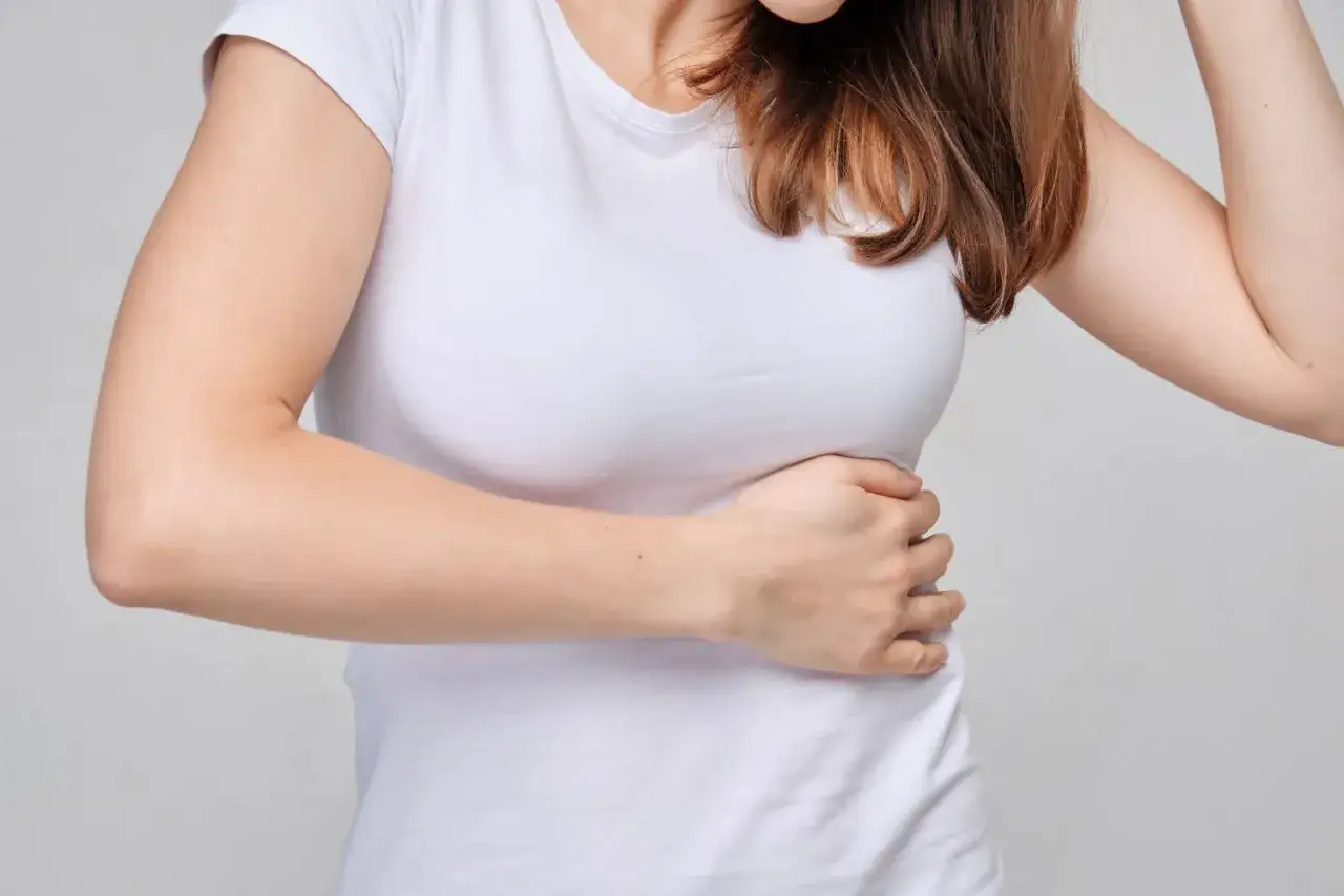 Kobieta w białej koszulce trzyma się za bok, odczuwając ból po lewej stronie brzucha.