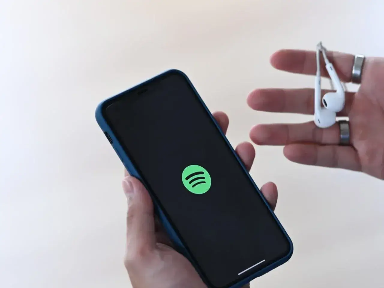 Dłoń trzyma smartfon z logo Spotify, a w drugiej dłoni słuchawki.