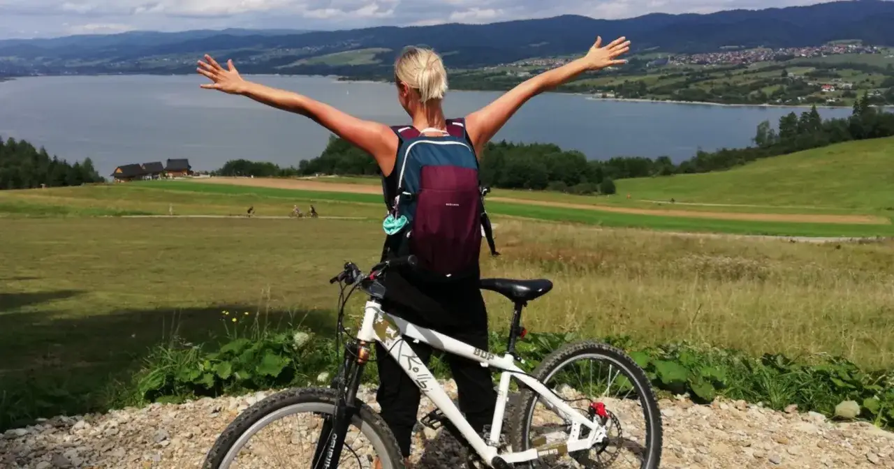 Kobieta z rowerem cieszy się pięknym widokiem na jezioro i góry. To są właśnie plusy jazdy na rowerze – wolność i kontakt z naturą.
