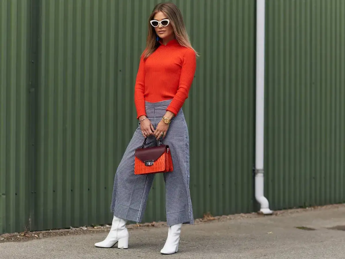 Spodnie kuloty dla jakiej sylwetki? Modelka w kraciastych spodniach kulotach i pomarańczowym golfie prezentuje stylową propozycję.