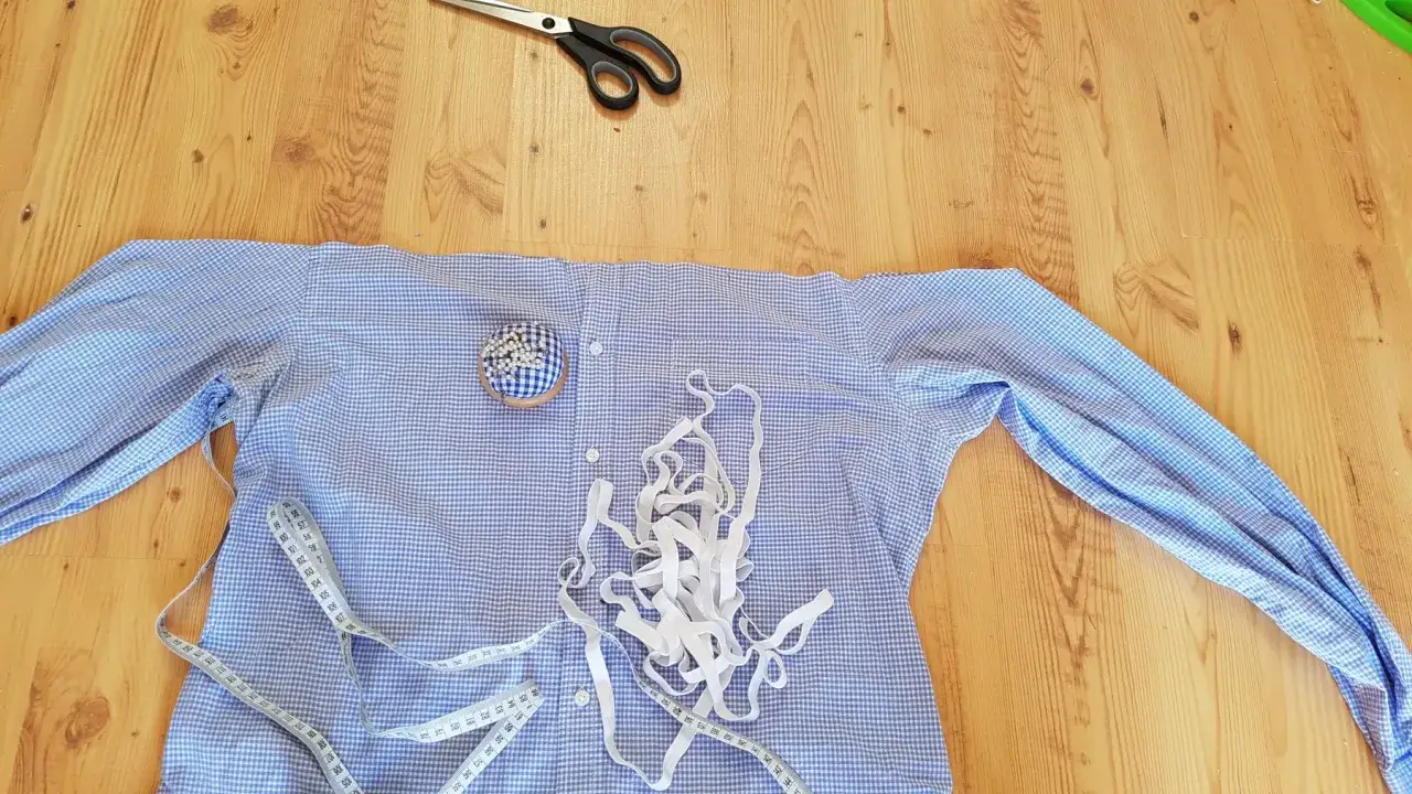 Przygotowania do przeróbki koszuli, by zmniejszyć bluzkę w ramionach. Nożyczki, miarka i szpilki czekają na pracę.