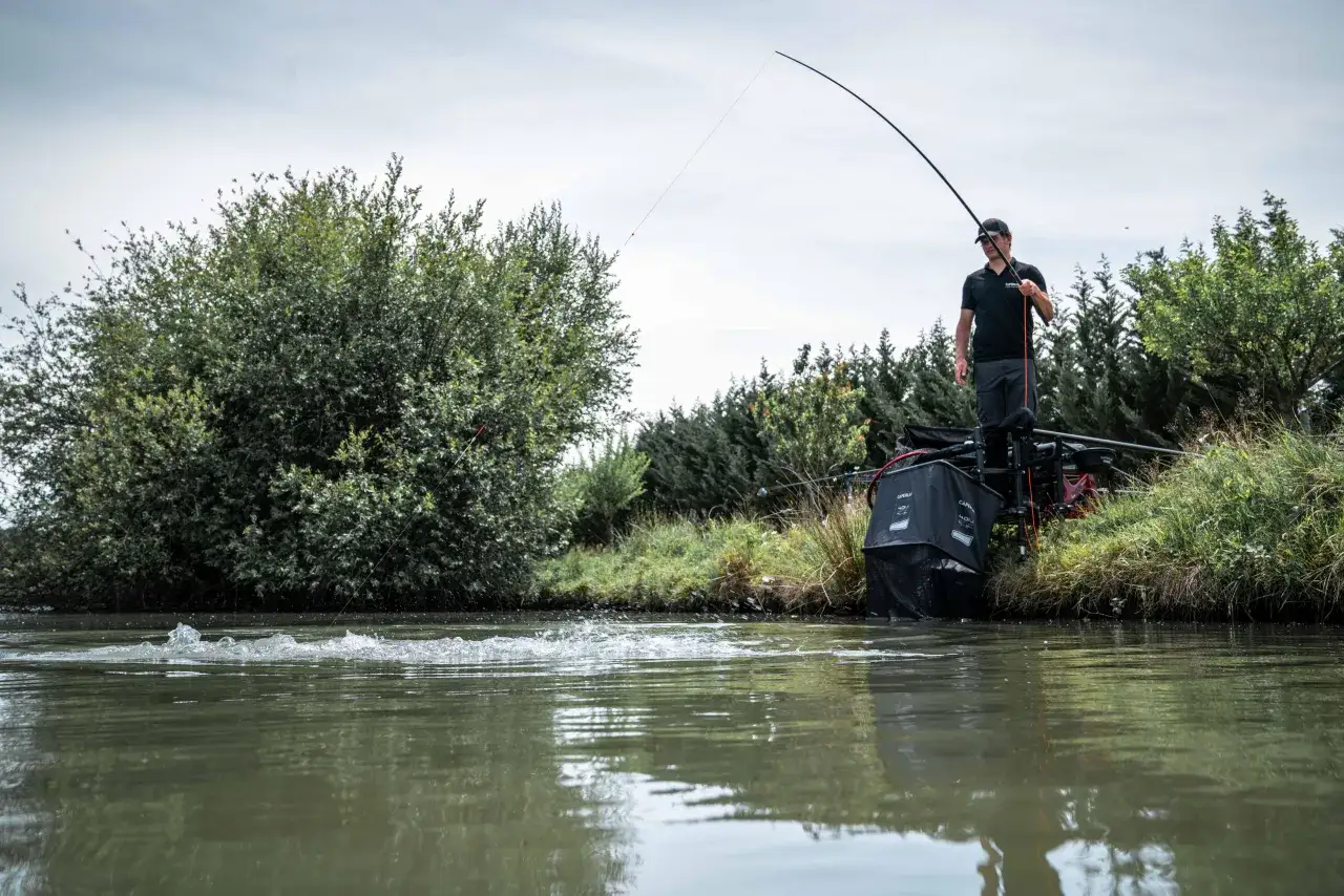 Wędkarz łowiący spinningiem na rzece, z podbierakiem i sprzętem wędkarskim.