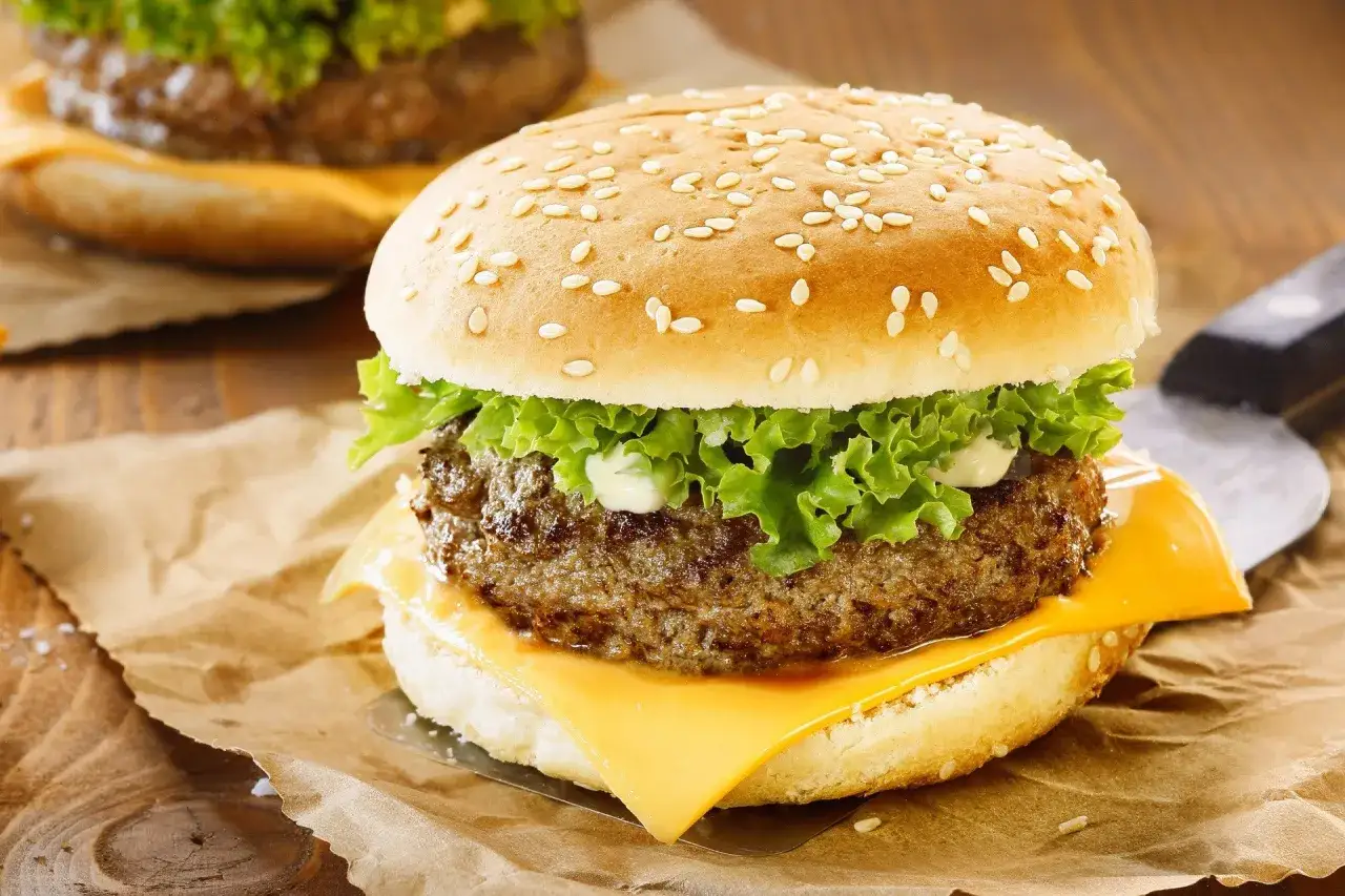 Zbliżenie na cheeseburgera z serem, sałatą i majonezem na bułce z sezamem.