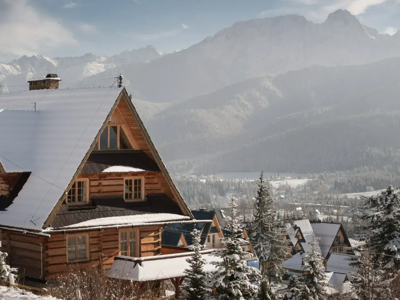 Zimowy krajobraz z nową bacówką w Zakopanem, otoczoną ośnieżonymi drzewami i górami w tle.