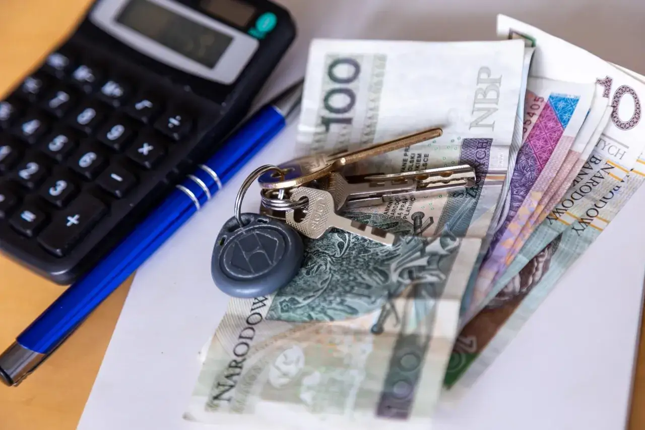 Klucze, pieniądze i kalkulator na biurku.