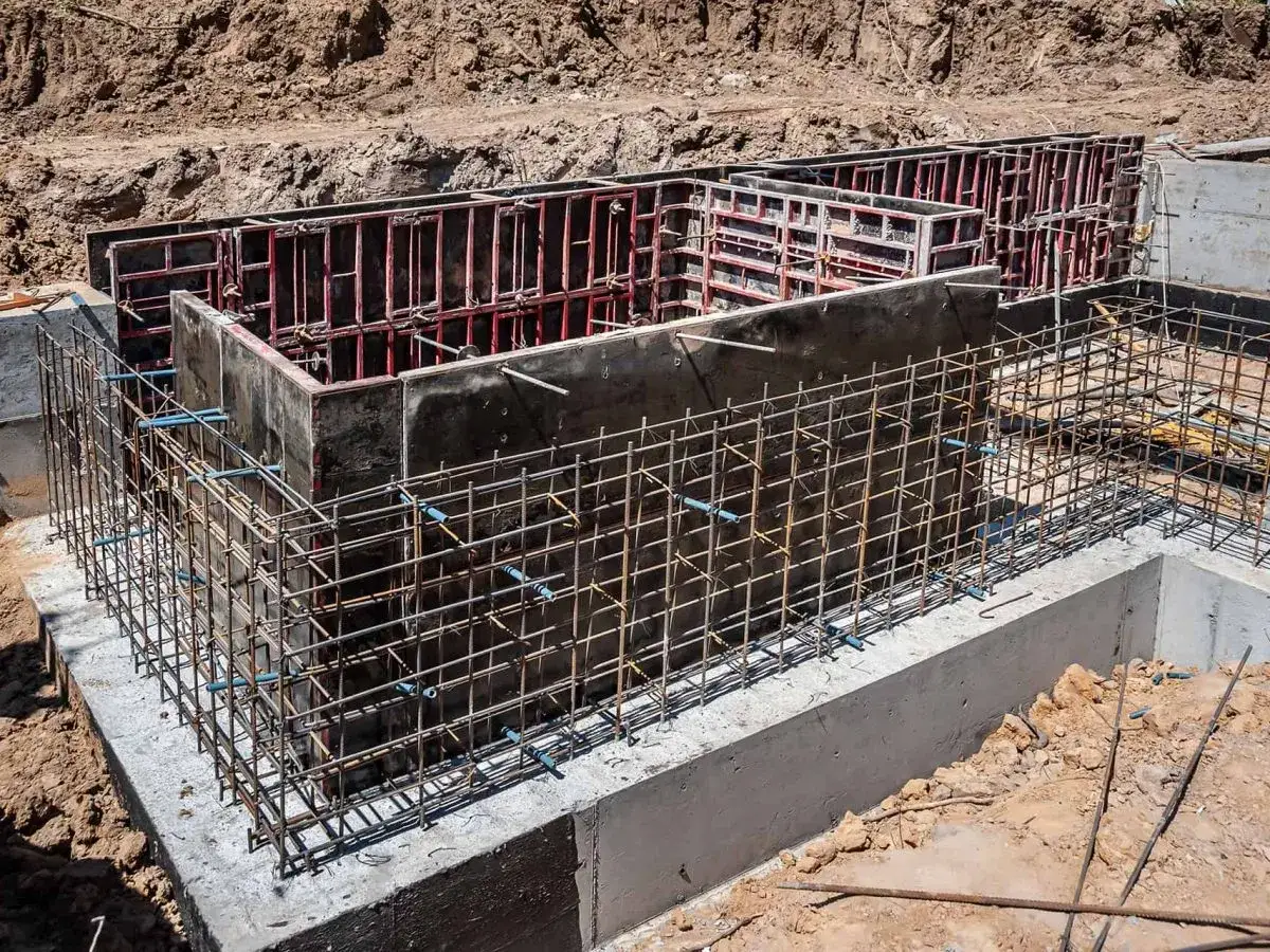 Siatka zbrojeniowa otacza betonowe szalunki, tworząc solidne zbrojenie ściany fundamentowej.