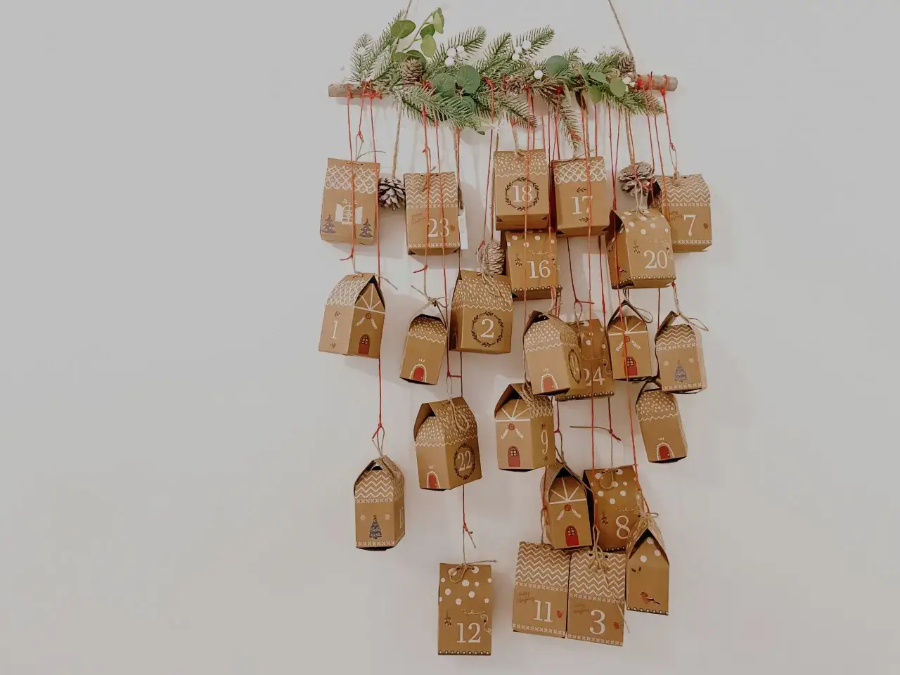 Uroczy pomysł na kalendarz adwentowy: zawieszone na gałęzi ozdobionej gałązkami jodły, małe, brązowe pudełeczka z numerami od 1 do 24.