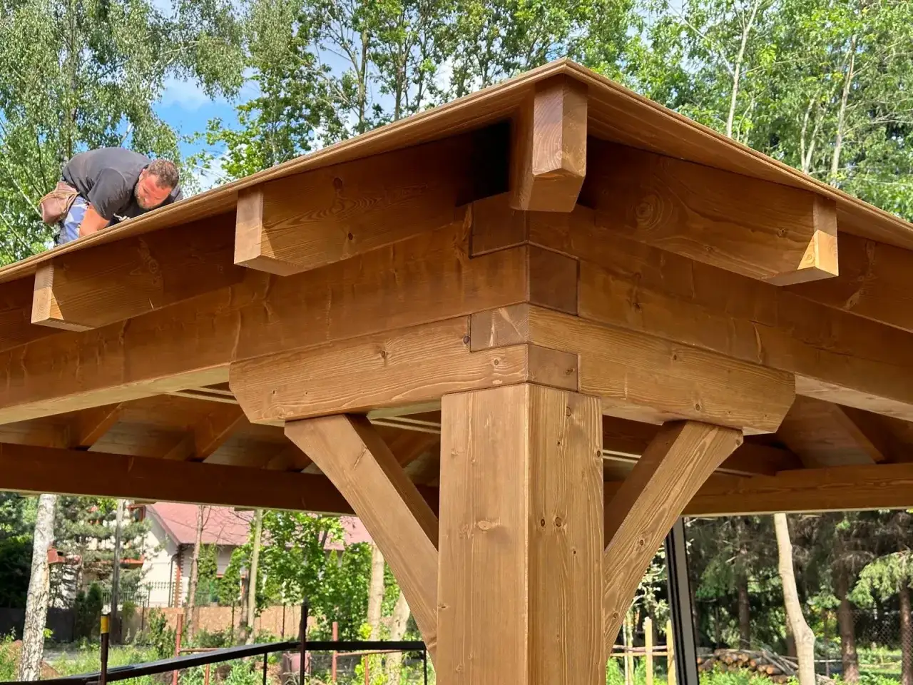 Budowa dachu kopertowego na altanie. Drewniana konstrukcja, pracownik montuje elementy.