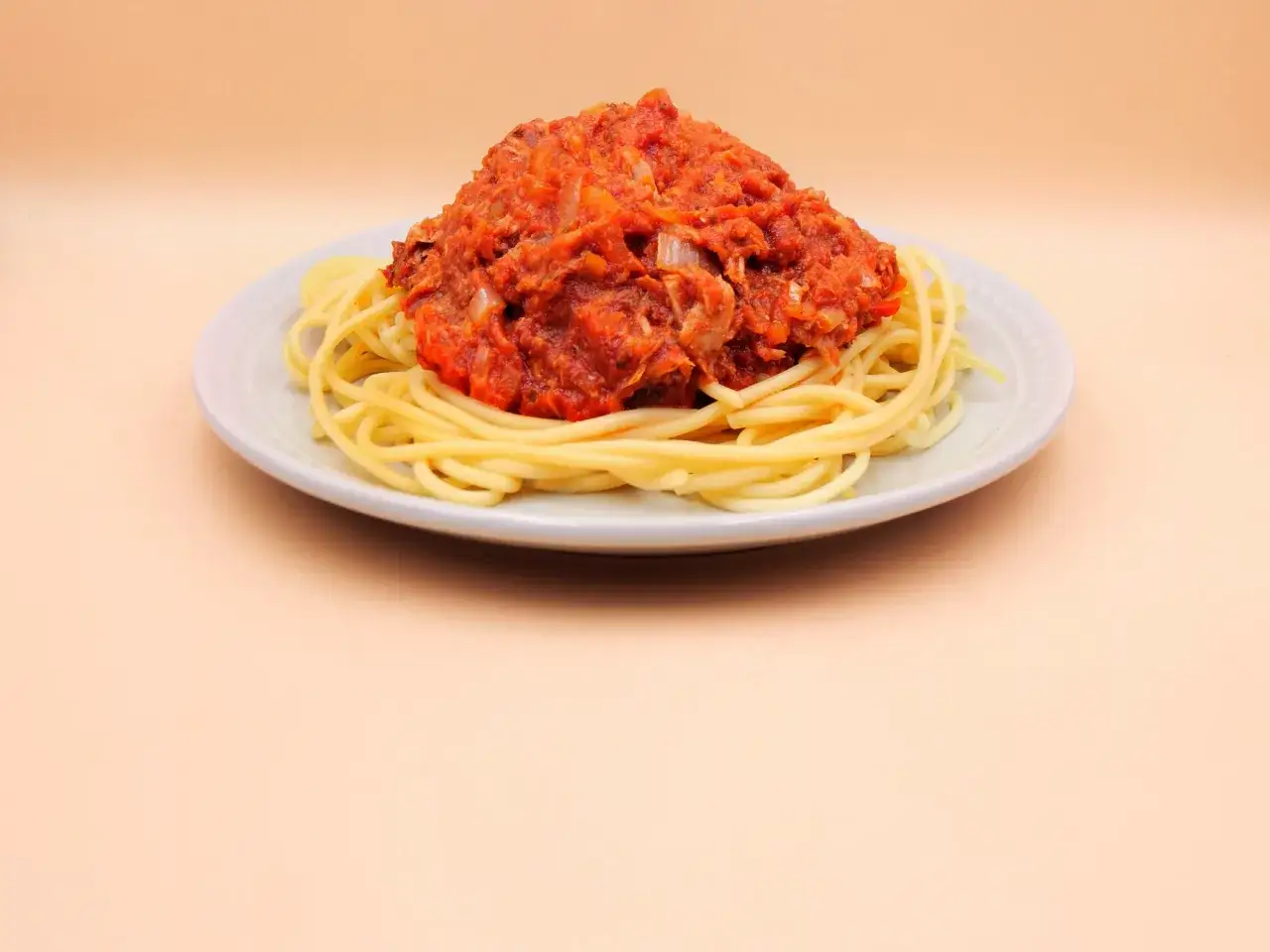 Porcja spaghetti z sosem pomidorowym i tuńczykiem, podana na jasnym talerzu.
