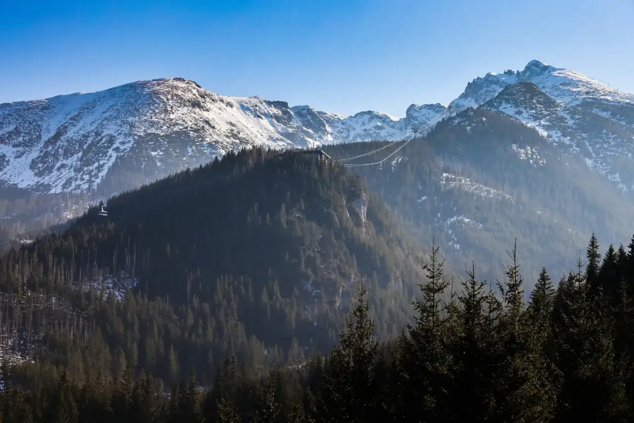 Zimowe Tatry, ośnieżone szczyty i gęste lasy. Kolejka linowa wznosi się ku górze, potwierdzając, czy w Tatrach opady są znacznie większe niż na nizinach.