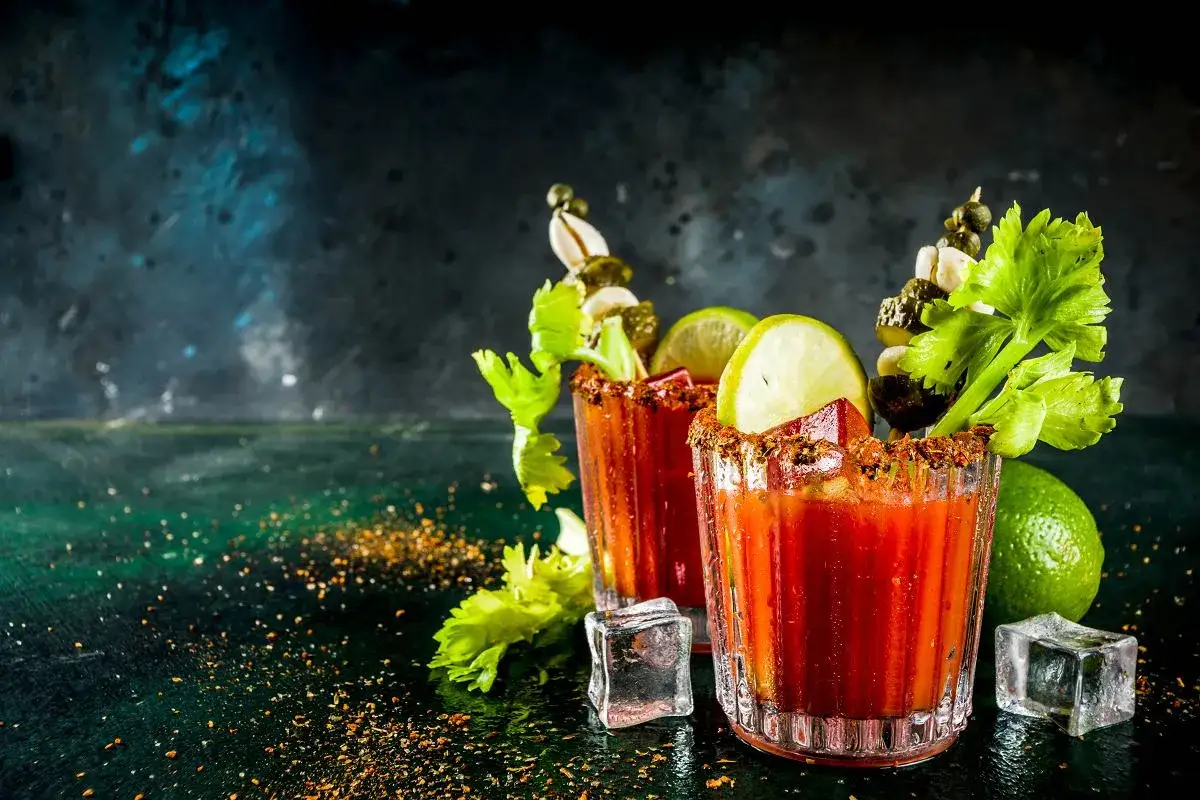 Dwa drinki Krwawa Mary z łodygami selera, limonką i piklami, ozdobione przyprawami i lodem.