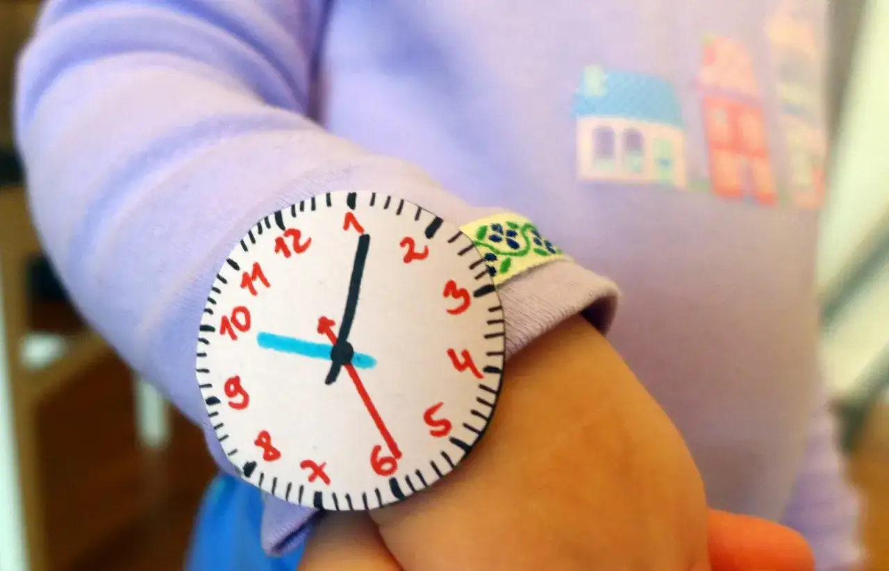 Jak zrobić wskazówki do zegara z papieru? Dziecko nosi na ręce własnoręcznie zrobiony zegarek z papieru.