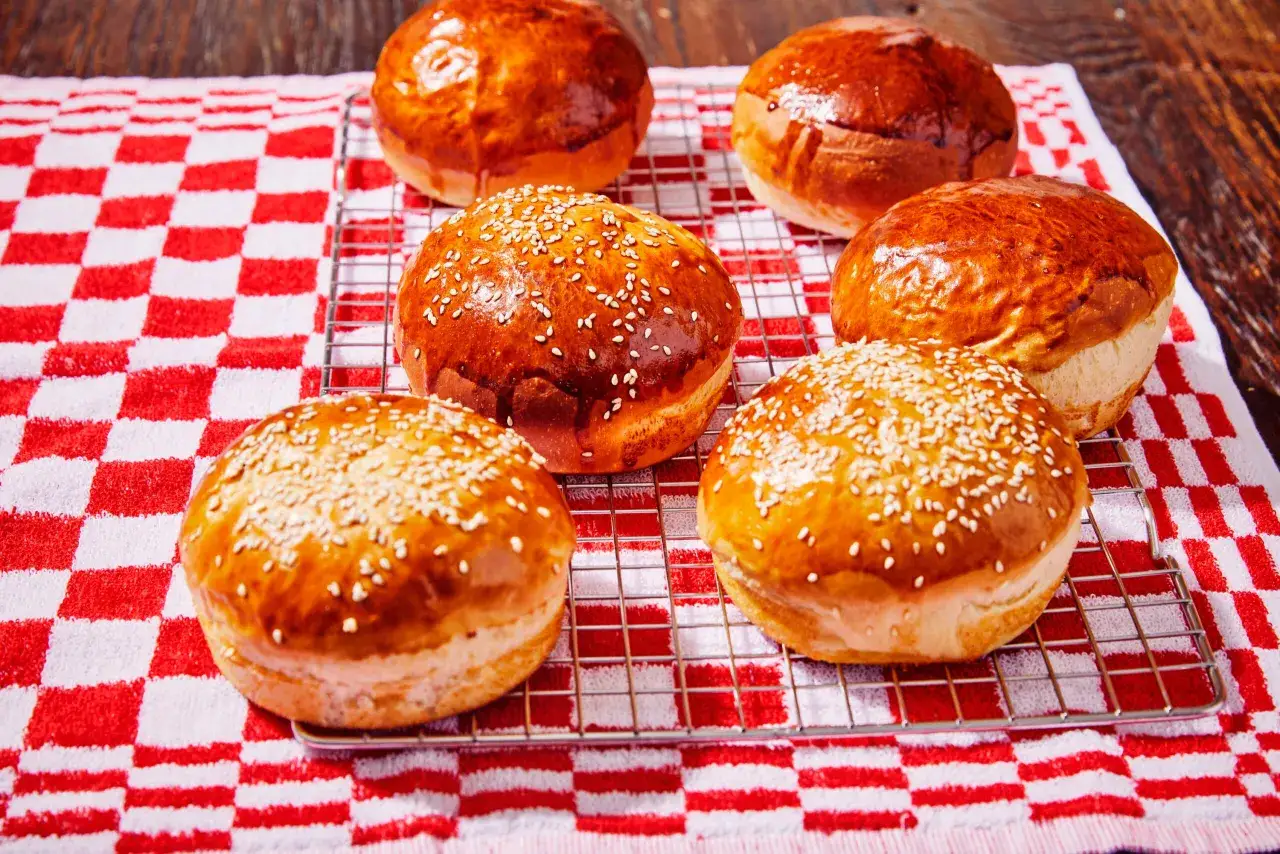 Petits pains à burger dorés et moelleux, certains parsemés de graines de sésame, sur une grille de refroidissement.