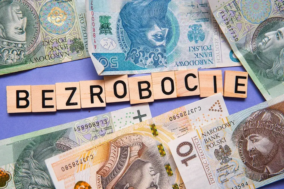 Litery układają się w słowo "BEZROBOCIE" na tle polskich banknotów. Zastanawiasz się, ile wynosi zasiłek dla bezrobotnych?