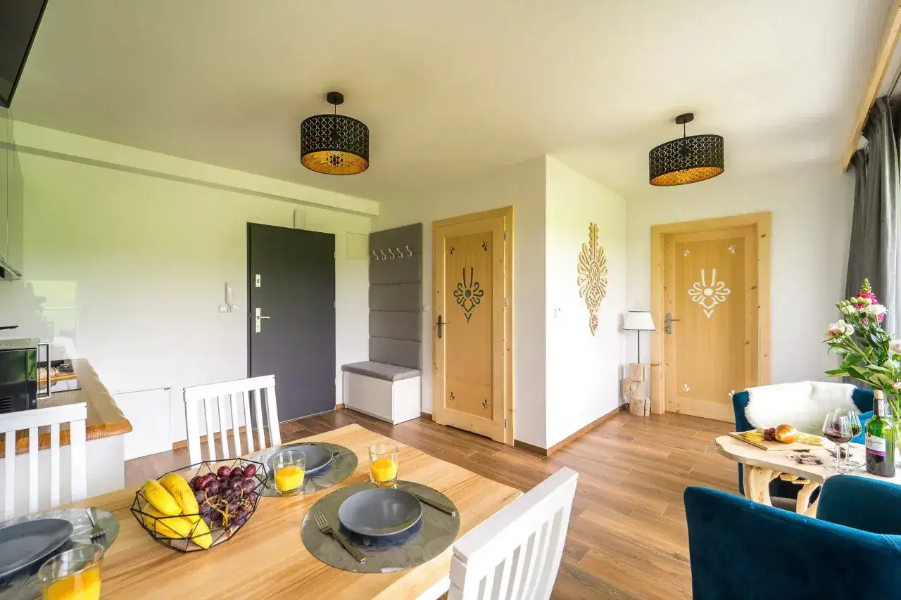 Pokoje gościnne Bachledzki Wierch: przytulne wnętrze z drewnianymi drzwiami, stołem z owocami i wygodnymi fotelami.