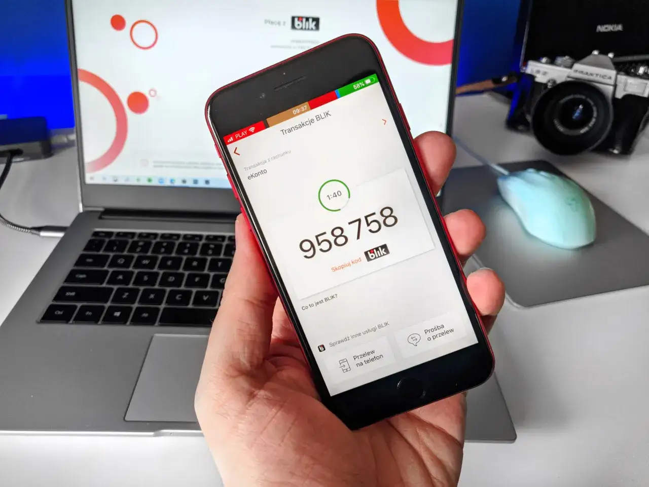 Dłoń trzyma smartfon z aplikacją Blik, na ekranie widoczny kod transakcji.