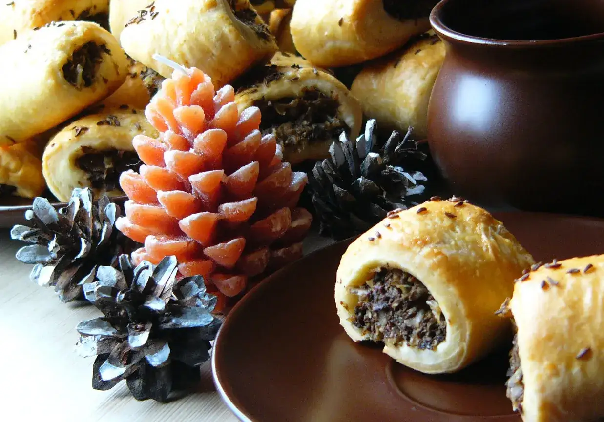 Paszteciki z grzybami i kminkiem, idealne do podgrzania. Obok świeca w kształcie szyszki i ozdobne szyszki.