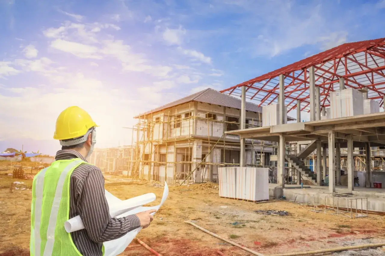 Inżynier w żółtym kasku i kamizelce odblaskowej analizuje plany budowy domu. Czy potrzebne jest pozwolenie na budowę?