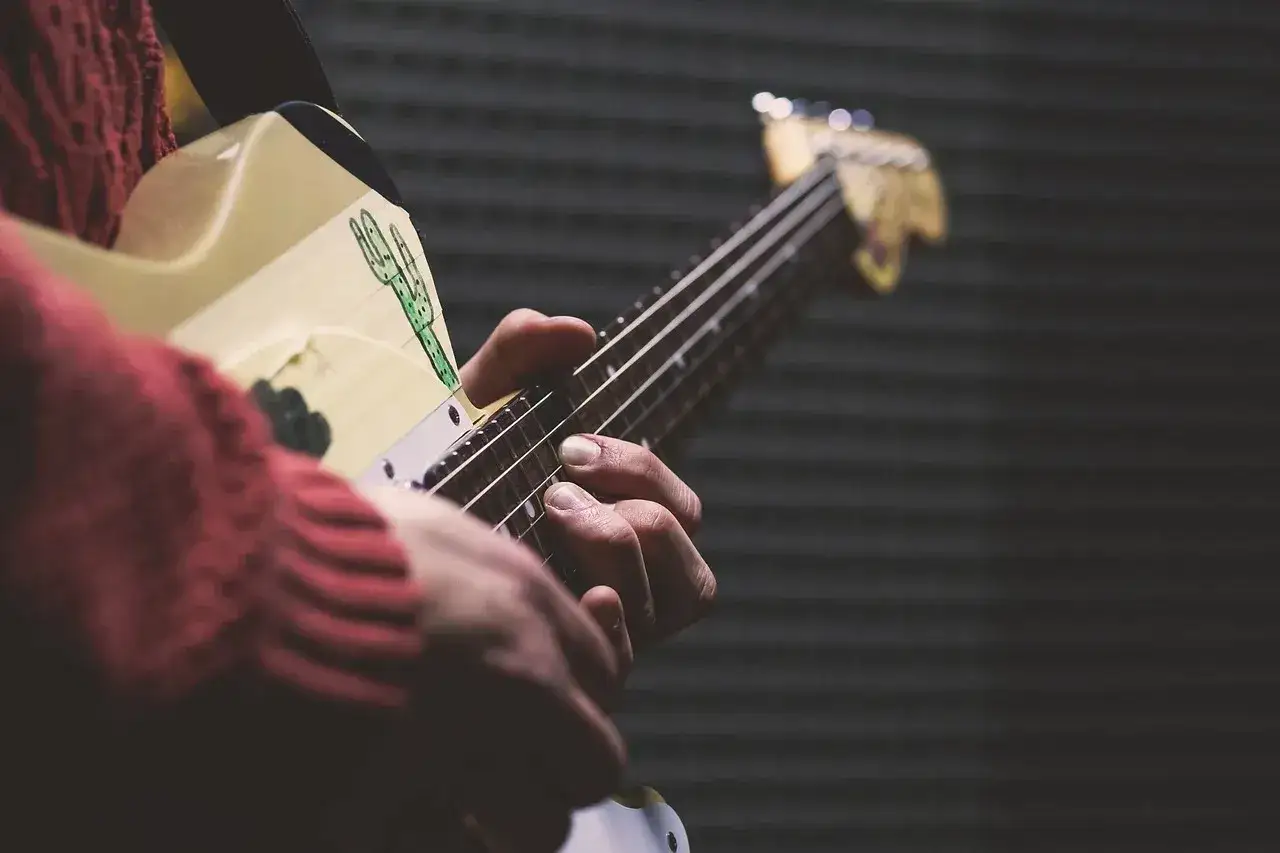 Dłonie grają na gitarze, ludowy instrument szarpany z rysunkiem kaktusa.