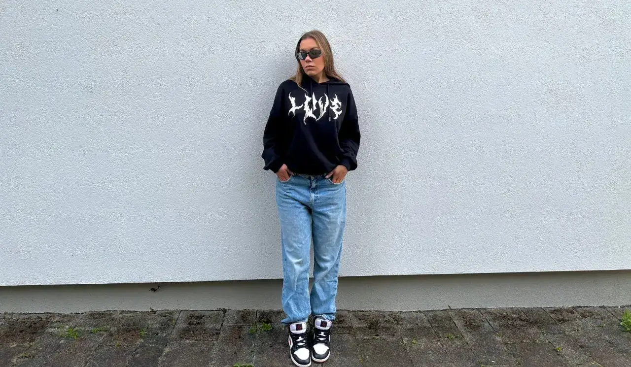 Dziewczyna w czarnej bluzie z kapturem i jeansach, idealny outfit, jak się ubrać na koncert hip hopowy.