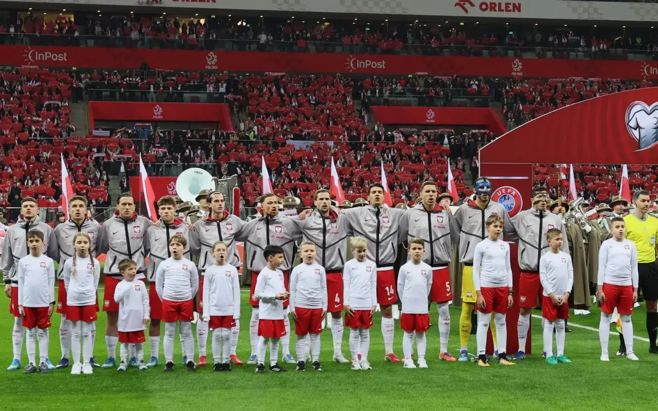 Piłkarze reprezentacji Polski i dzieci stoją na murawie stadionu, w tle trybuny z kibicami.