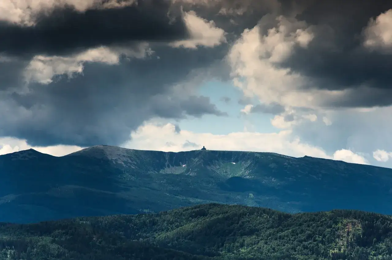 Majestatyczne, najwyższe pasma górskie w Polsce pod burzowym niebem. Na szczycie widać niewielki budynek.