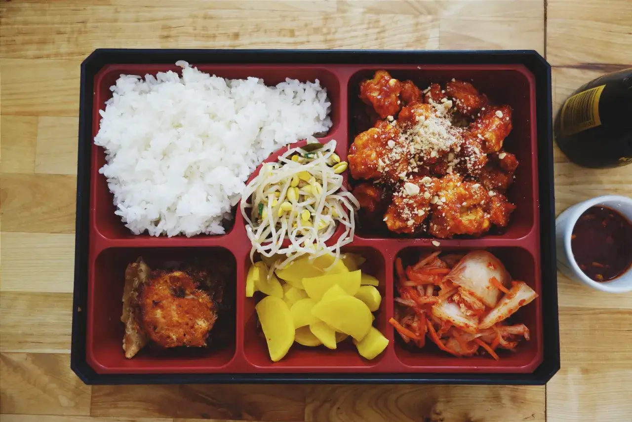Bento box z ryżem, kurczakiem w sosie, kimchi, fasolką i żółtą rzodkiewką.