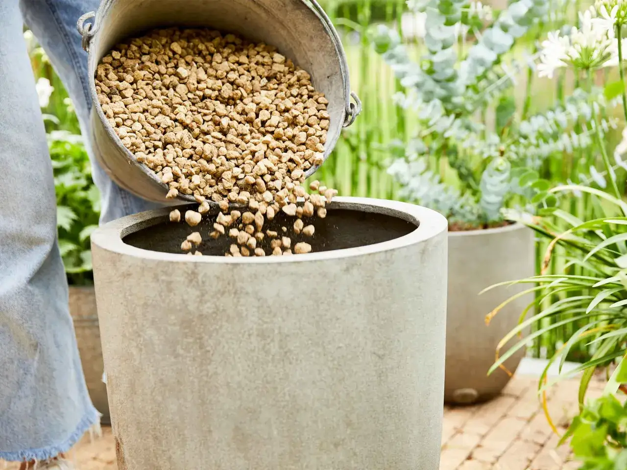 Wsypywanie keramzytu do doniczki, by zrobić drenaż. To kluczowy krok, jak zrobić drenaż w doniczce, zapewniający zdrowie roślin.