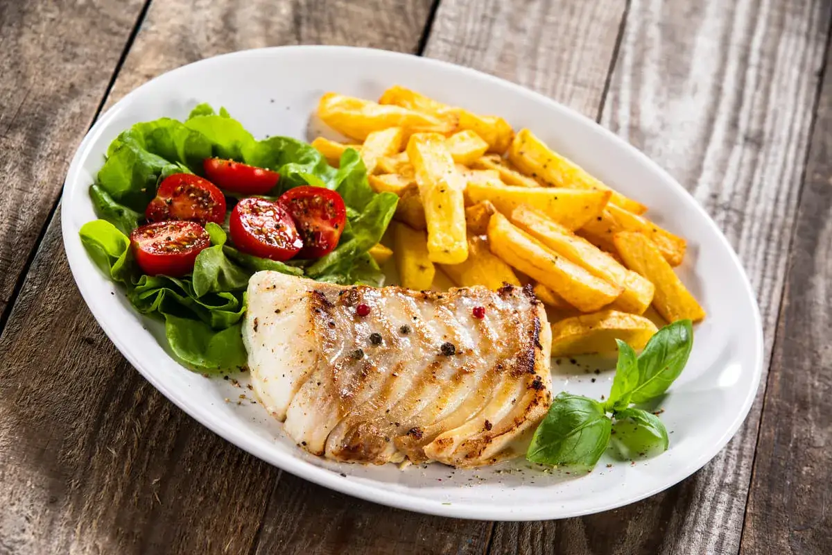 Idealne jakie przyprawy do ryby? Pieprz i sól na grillowanym filecie, obok frytki i sałatka z pomidorkami.