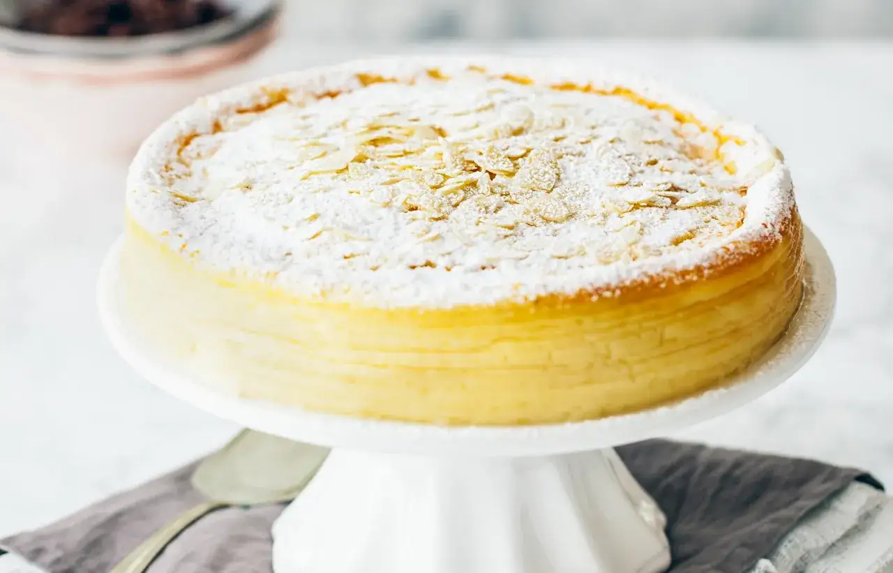 Idealny sernik który nie opada, ania gotuje z płatkami migdałów i cukrem pudrem na białej paterze.