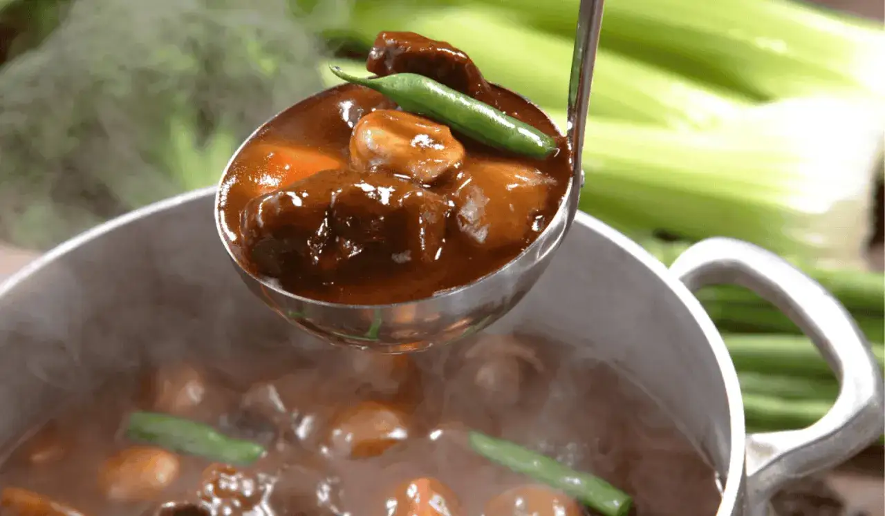 A ladle scoops tender, slow-cooked meat in rich gravy from a steaming pot. Perfect for learning jak dusić mięso.